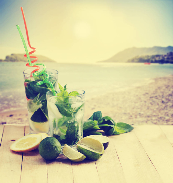 mojito cocktails with straws on wooden table with beach on background - Foto, Imagen