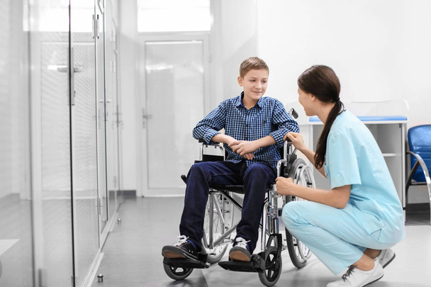 Young female doctor taking care of man in wheelchair indoors - Foto, afbeelding