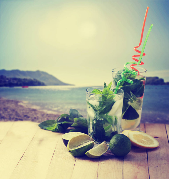 mojito cocktails with straws on wooden table with beach on background - Foto, Imagen