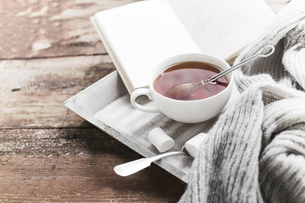 cup of hot tea and book on wooden surface - Photo, Image