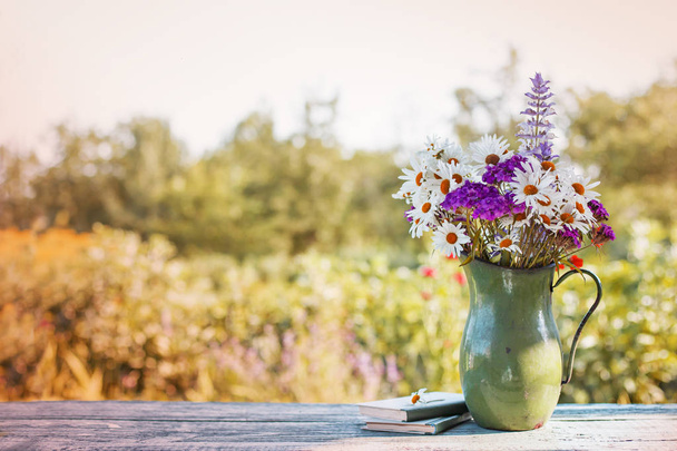 wild flowers in vase standing over wooden table with blurred nature background - Фото, зображення