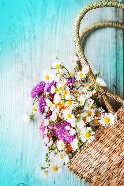 bouquet of colorful wild flowers in upturned basket on blue wooden table - Fotografie, Obrázek