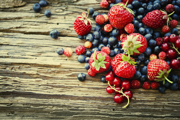 heap of fresh ripe blueberries and strawberries on wooden surface - Photo, Image