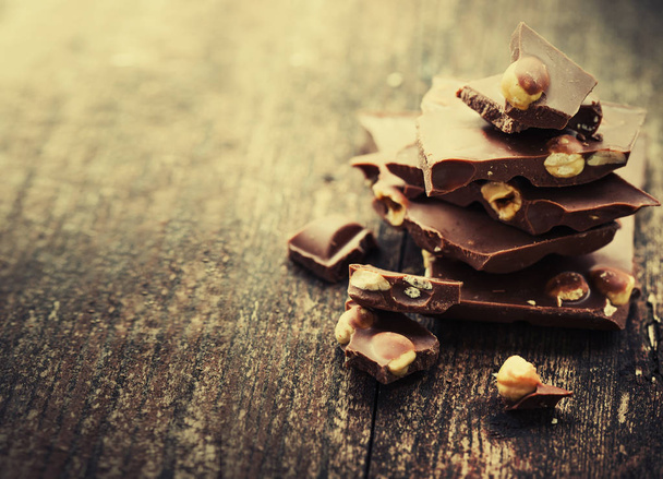 Broken chocolate with nuts on wooden background - Foto, imagen