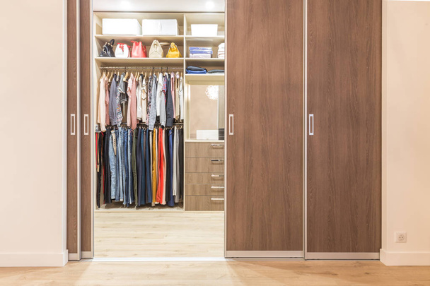 Armario moderno de madera con ropa colgando en el carril en el walk in closet
 - Foto, imagen