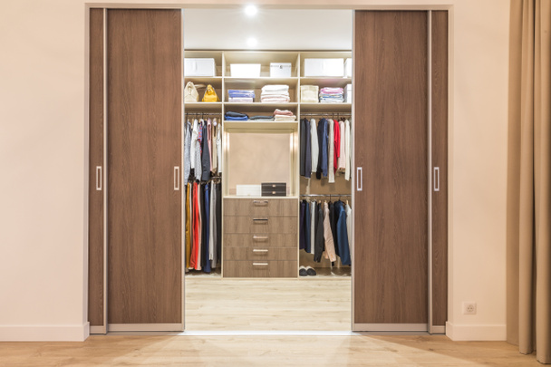 Modern wooden wardrobe with clothes hanging on rail in walk in closet - Photo, Image