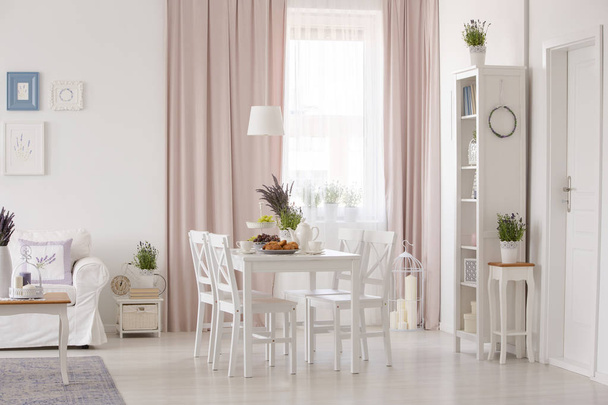 White chairs at table near couch in pink apartment interior with drapes and plants. Real photo - Fotó, kép