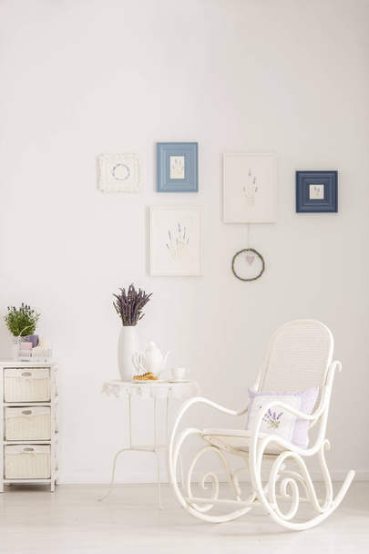 Rocking chair next to table with lavender flowers in white living room interior with posters. Real photo - Photo, image