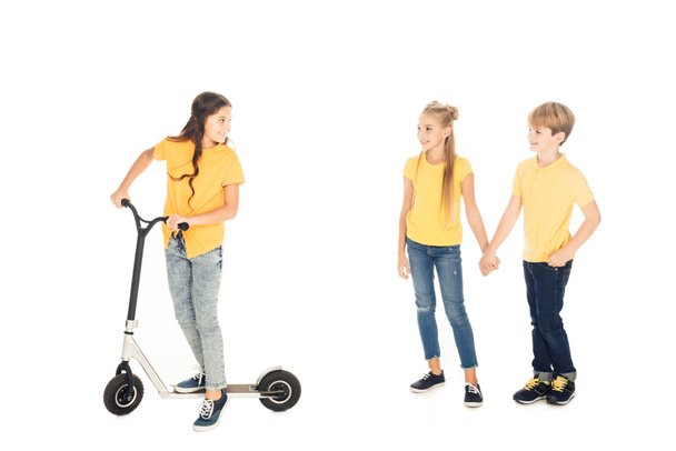 happy child riding scooter and looking at friends holding hands isolated on white - Foto, immagini