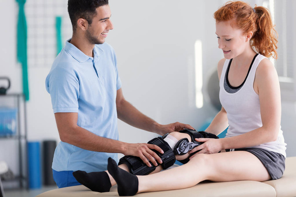 Happy physiotherapist supporting patient with stiffener on the leg - Photo, image