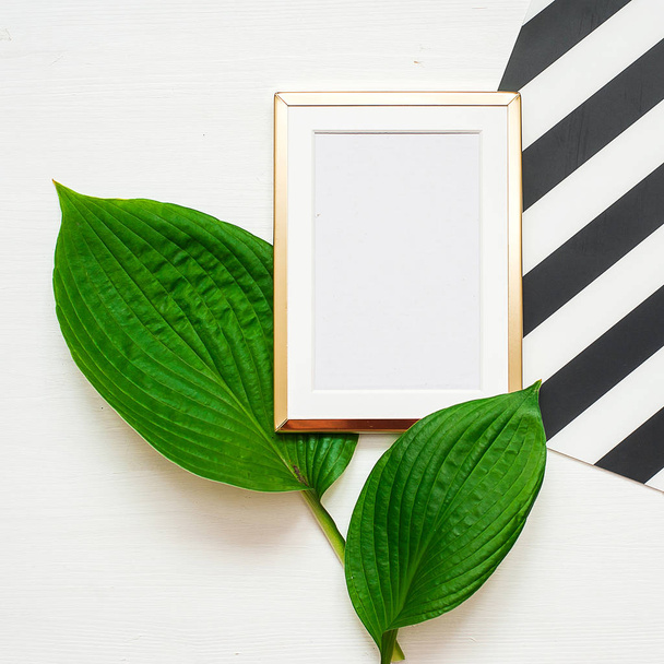 Gold photo frame with tropical leaves on black and white striped background. Mock up frame with copyspace. Flat lay, top view. - Fotoğraf, Görsel