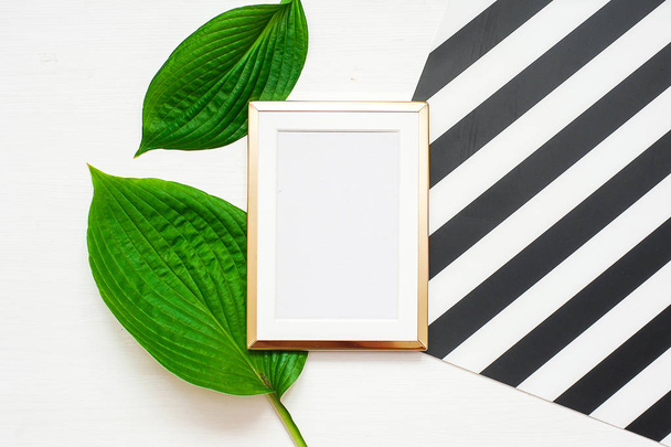 Gold photo frame with tropical leaves on black and white striped background. Mock up frame with copyspace. Flat lay, top view. - Фото, зображення