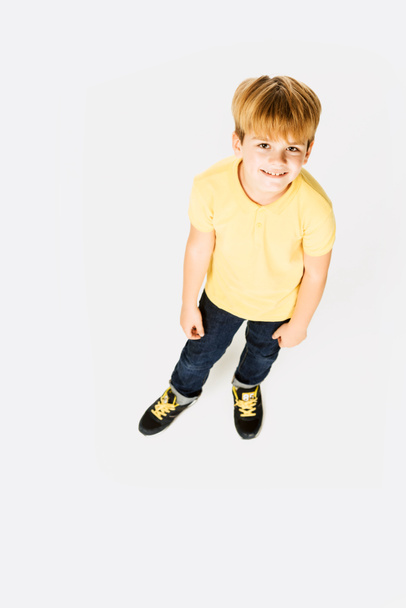 high angle view of adorable happy little boy standing and smiling at camera isolated on white - Foto, Imagem