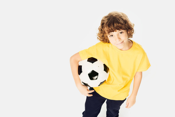 high angle view of little boy holding soccer ball and smiling at camera isolated on white  - Фото, изображение