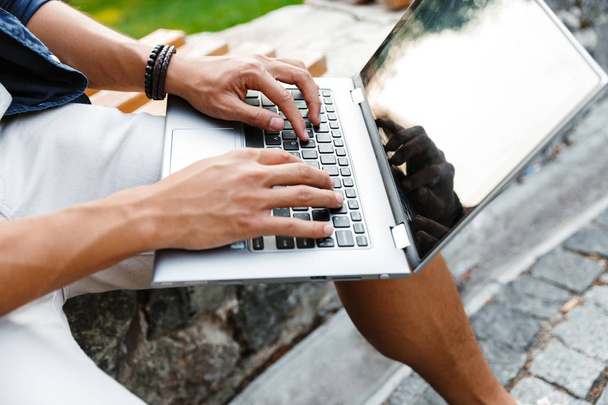 Cropped image of asian male student using laptop computer while sitting on bench in park - Photo, image
