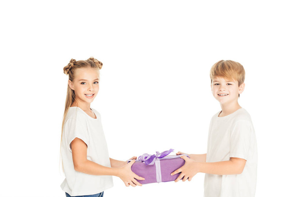 Çocuk sunan hediye kutusu beyaz ve onlar kameraya bakarak izole arkadaşına gülümseyen - Fotoğraf, Görsel