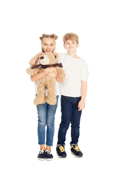 smiling kids hugging, holding teddy bear and looking at camera isolated on white - Photo, Image