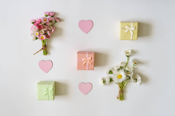 Summer creative composition. Two white and pink Marguerite daisy flowers bouquets, three small gift boxes in pastel colors and three pink hearts on white background. Top view, flat lay - Foto, Imagen
