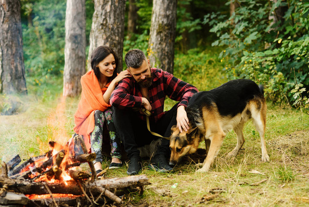Couple with german shepherd dog near bonfire, forest background. - Foto, imagen