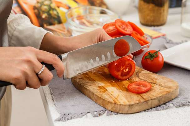 Closeup of female hands cutting tomatoes for salad on wooden board with knife - Photo, Image