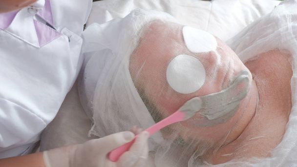 Procedimento terapêutico de limpeza e elevação da pele facial. O cosmetologista mancha uma máscara de alginato de cor cinza na bochecha de uma mulher gorda
. - Foto, Imagem