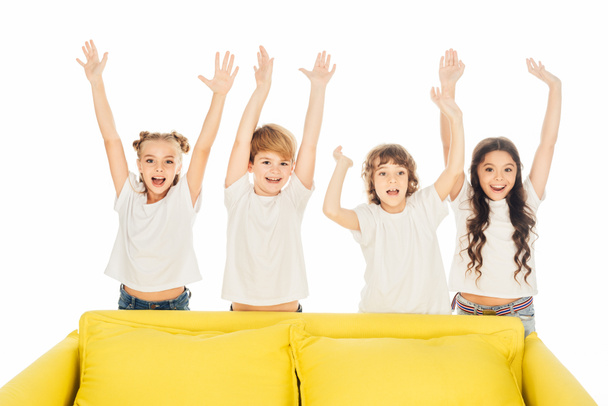 白で隔離の上げられた手で黄色のソファの後ろに立って幸せな子供 - 写真・画像