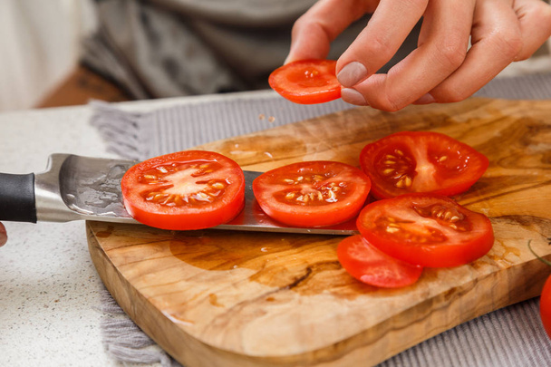 Primo piano di mani femminili che tagliano pomodori per insalata su asse di legno con coltello
 - Foto, immagini
