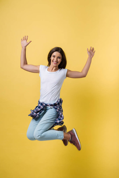 Full length portrait of a cheerful casual caucasian woman jumping isolated over yellow background - 写真・画像