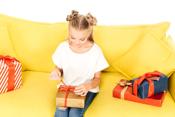 high angle view of adorable child opening present on yellow sofa isolated on white - Foto, Imagem