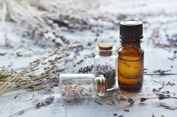 natural organic lavender oil in small glass bottle and dried lavender flowers over wooden background - Zdjęcie, obraz