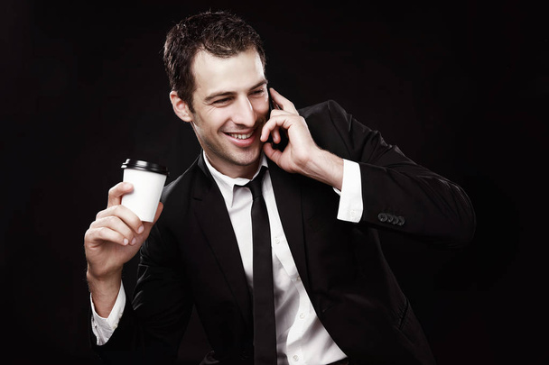 Brutální chlapík v černém obleku s kávou a telefonem. Černé pozadí. Kávu s sebou. Manažer - Fotografie, Obrázek