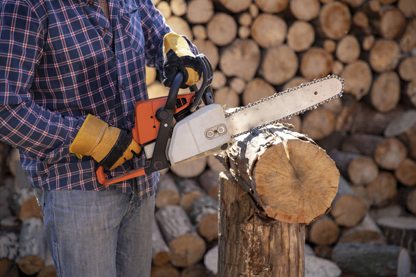 The worker works with a chainsaw. Chainsaw close up. Woodcutter saws tree with chainsaw on sawmill. Chainsaw in action cutting wood. Man cutting wood with saw, dust and movements. - Фото, зображення