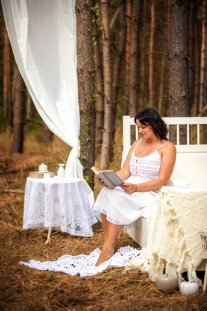 Woman is reading book in bed in the morning on the nature background of forest - Photo, Image