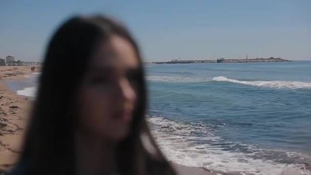 ein verschwommenes Porträt eines Mädchens vor malerischem Blick auf Strand und Meer an klaren, sonnigen Tagen. setzt das Mädchen eine Sonnenbrille auf. Der Fokus verlagert sich vom Hintergrund auf das Mädchen. Meereswellen spiegeln sich in den Schatten - Filmmaterial, Video
