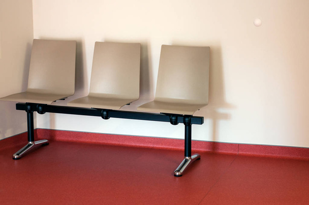Primer plano de la alineación de la silla beige en el suelo rojo en una sala de espera
 - Foto, Imagen