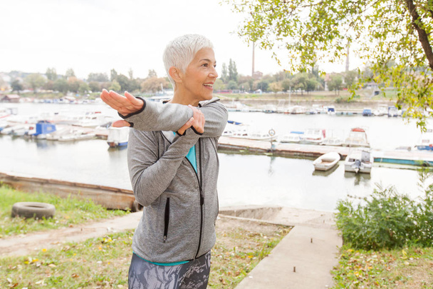 Mujer mayor activa en ropa deportiva haciendo ejercicio físico, entrenamiento al aire libre
. - Foto, Imagen