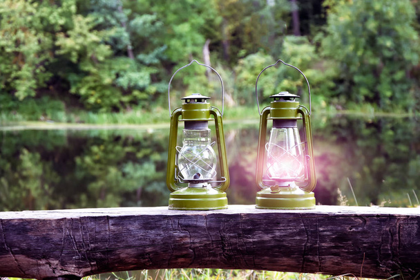Dos lámparas de queroseno. Una antigua lámpara de aceite quema bosque de hadas contra el fondo del río. Símbolo amor romance en estilo rústico
 - Foto, Imagen