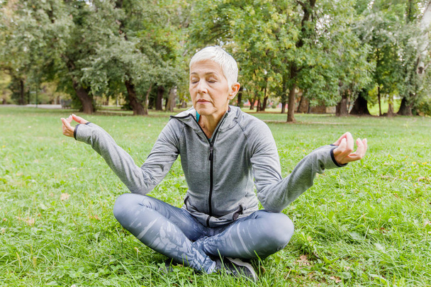 Porträt einer Seniorin entspannt in Yoga-Pose auf grünem Gras im Park. - Foto, Bild