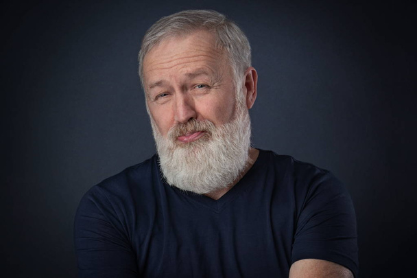 alter Mann mit grauem Bart posiert mit verachteter Fratze im Studio - Foto, Bild