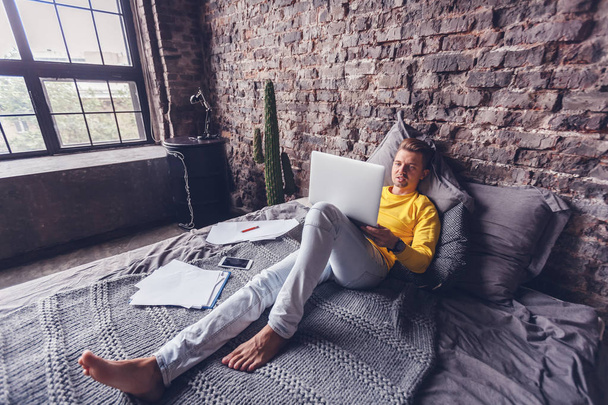 Jonge man aan het werk op laptop thuis liggen op bed, freelancer, digitale werknemer, entertainment en internet - Foto, afbeelding