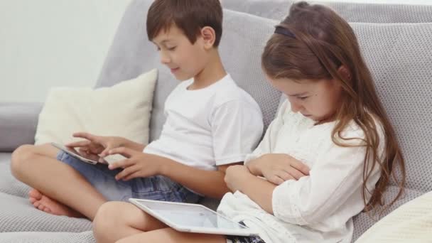 Two kids with gadgets. Sister and brother surfing the net or playing online games on digital tablets at home. Side view - Video, Çekim