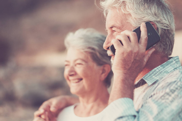 šťastný starší pár s mobilní telefon na oblázkové pláži, smáli se a žertovali - Fotografie, Obrázek