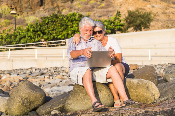 счастливая пожилая пара с планшетным компьютером на галечном пляже смеется и шутит
 - Фото, изображение