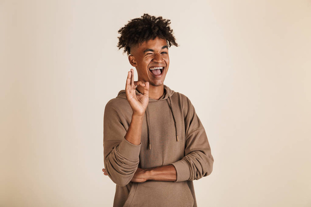 Portrait of a smiling young afro american man dressed in hoodie showing ok isolated - Valokuva, kuva