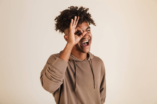 Portrait of a cheerful young afro american man dressed in hoodie showing ok isolated - Foto, imagen