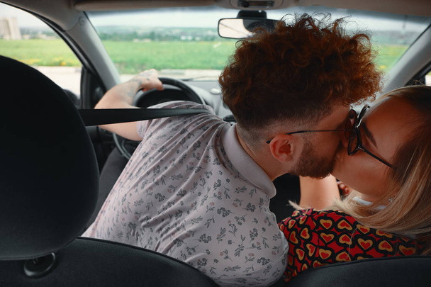 Güzel genç çift arabanın ön koltukta öpüşme. Havada aşktır. Arkadan görünüm. Kucaklamak ve onun güzel kız arkadaşı bir yol gezisi sırasında öpüşme genç adam. - Fotoğraf, Görsel