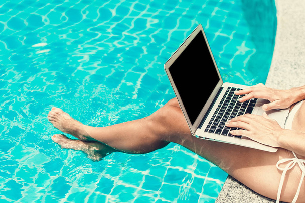 Woman freelancer working on her laptop computer sitting at poolside - 写真・画像