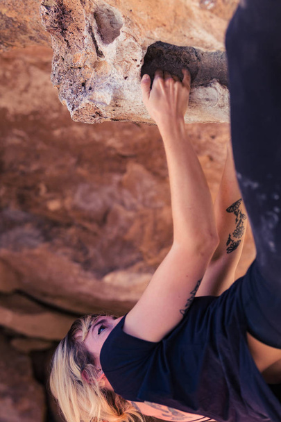 Femme caucasienne blonde mince avec des tatouages de bras pend à l'envers tandis qu'elle escalade des rochers sur des rochers dans le désert de Californie
 - Photo, image