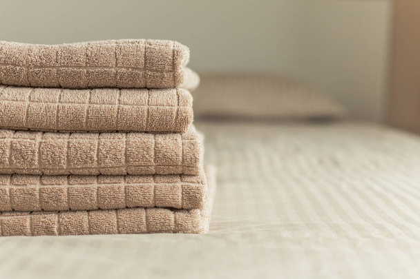 Stack of beige hotel towel on bed in bedroom interior. Vintage toning. Soft focus. - Fotó, kép