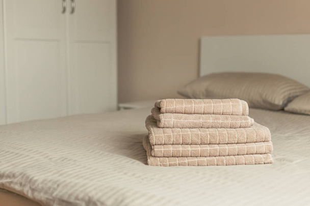 Stack of beige hotel towel on bed in bedroom interior. Vintage toning. Soft focus. - Фото, изображение